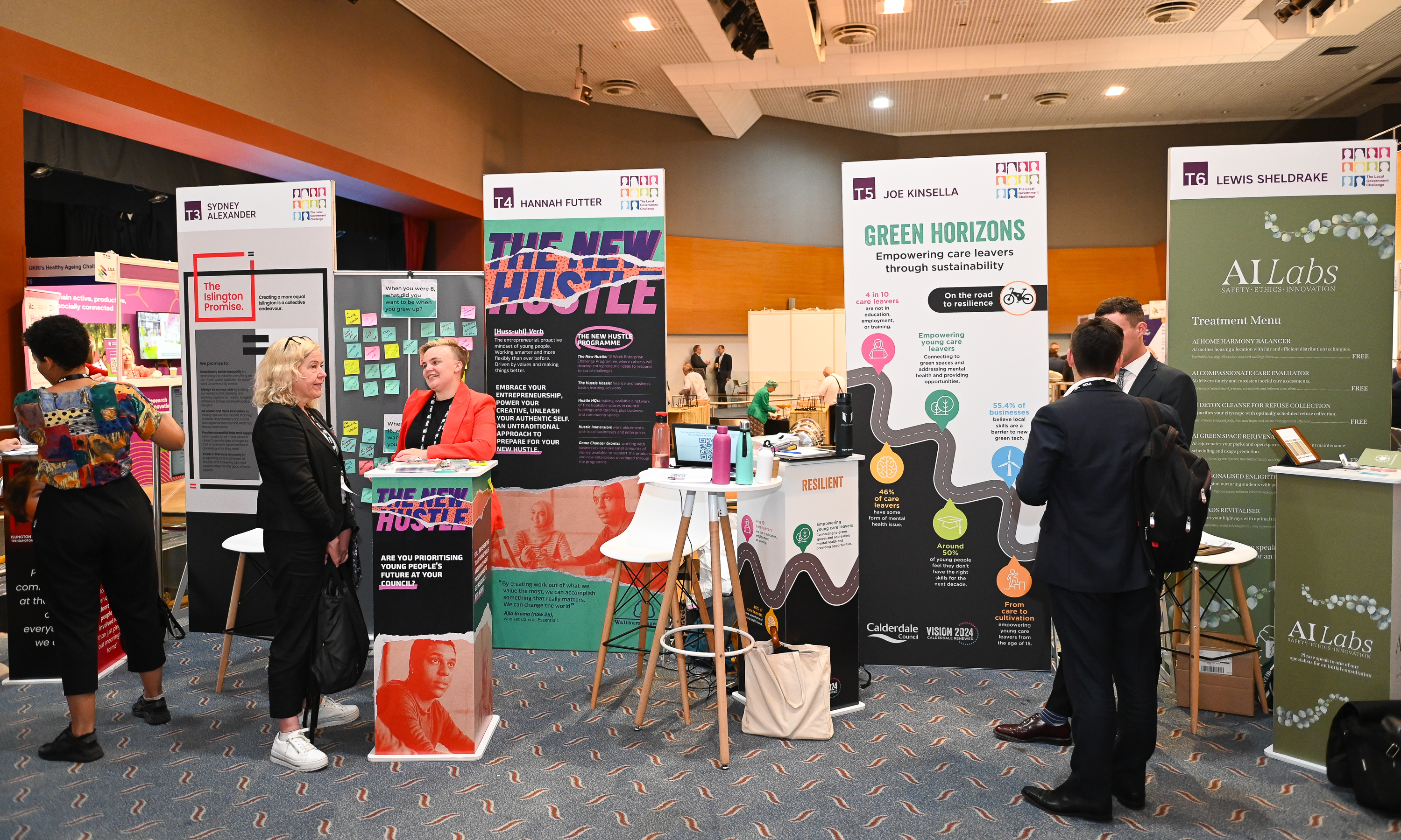 Four exhibition stands in a large conference room with people talking. 
