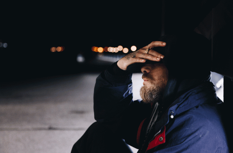 Homeless man sitting on the street and covering his eyes