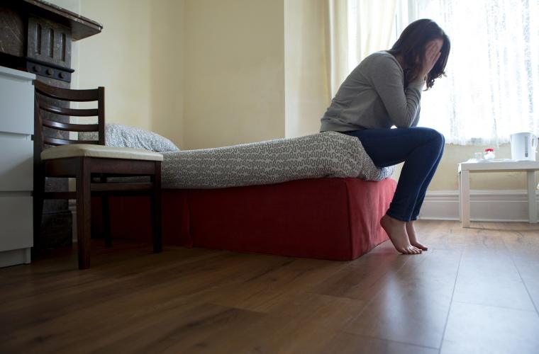 Woman sat on the end of her bed looking distraught
