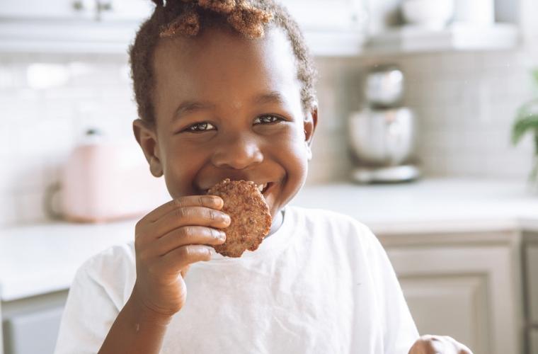 Young boy wearing a white t-shirt eating a cookie in a white decorated kitchen