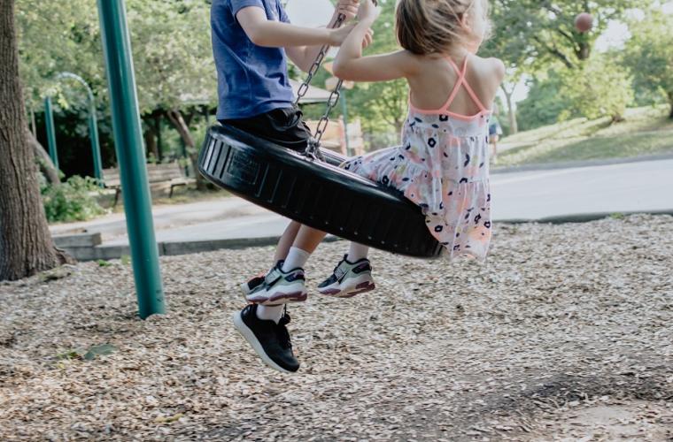  boy in green top and girl in white dress playing on swing