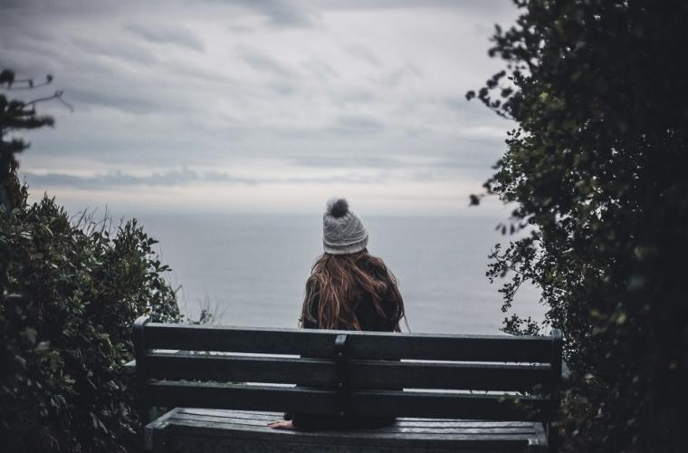 Girl sitting on a bench wearing a woolly hat looking out to sea