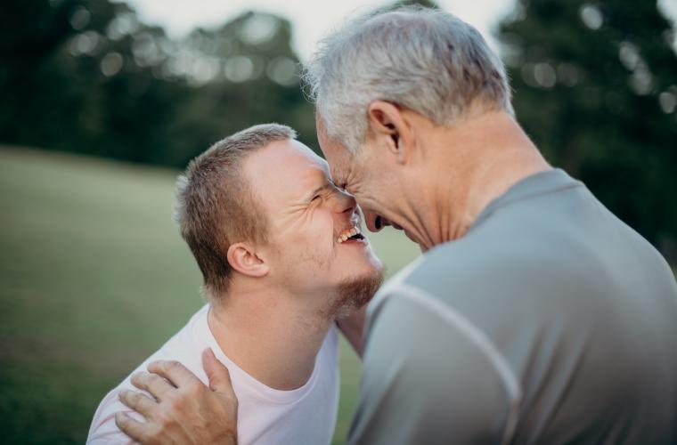 Older white man hugging a younger white boy who has learning disabilities, they are both smiling