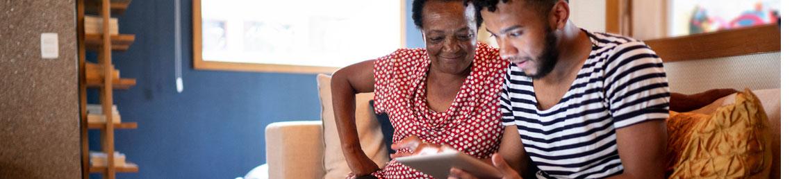Black woman and a disabled black man sitting on a sofa using an ipad 